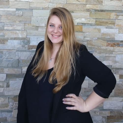AnneMarie Austin, wedding planner and owner, smiling in a black outfit against a stone wall background, representing professional expertise in wedding planning.