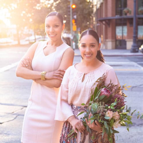 Paula and Anjelica, professional event planners, posing confidently outdoors, showcasing creativity and teamwork in event management.