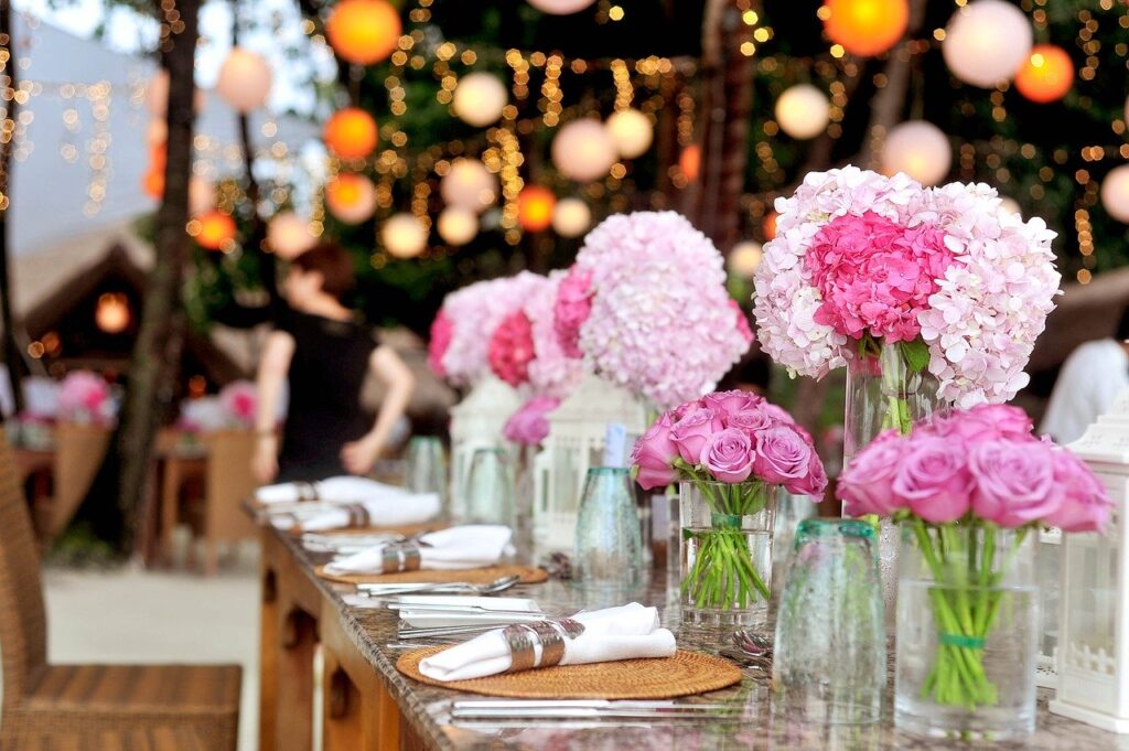 Elegant table setting with pink and white floral arrangements, lanterns, and twinkling lights, ideal for wedding or party ambiance, enhancing event experiences.