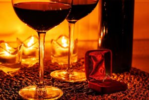 Glasses of red wine beside a wine bottle and a red velvet ring box, creating a romantic atmosphere for holiday events and celebrations.