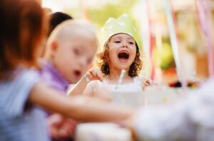 Child wearing a party hat joyfully celebrating at a festive event, surrounded by other children, capturing the lively atmosphere of holiday gatherings enhanced by photo booth experiences.