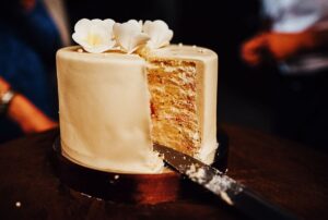 Cake with a slice removed, decorated with white flowers, set on a wooden table, symbolizing celebration and event enjoyment for parties.