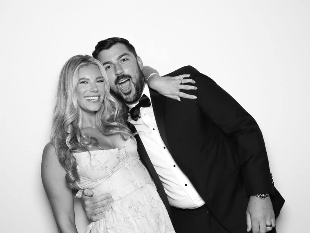 Couple joyfully posing together, embracing with playful smiles, showcasing a cozy and loving connection, perfect for capturing memorable moments in a photo booth setting.