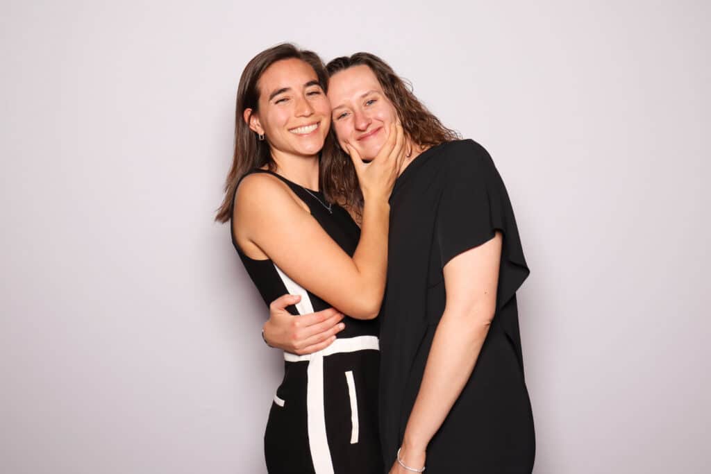 Two women smiling and embracing in a playful photo booth pose, showcasing a cozy and joyful connection, ideal for capturing memorable moments in couples' photography.