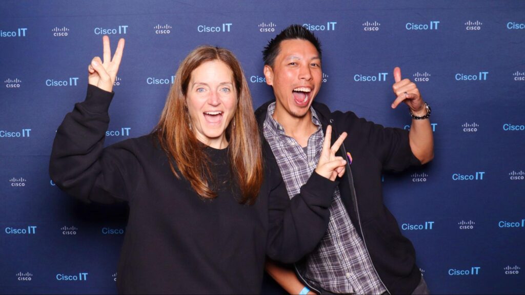 Two smiling individuals posing playfully in front of a branded Cisco IT backdrop, showcasing engagement and enjoyment at a corporate event photo booth.