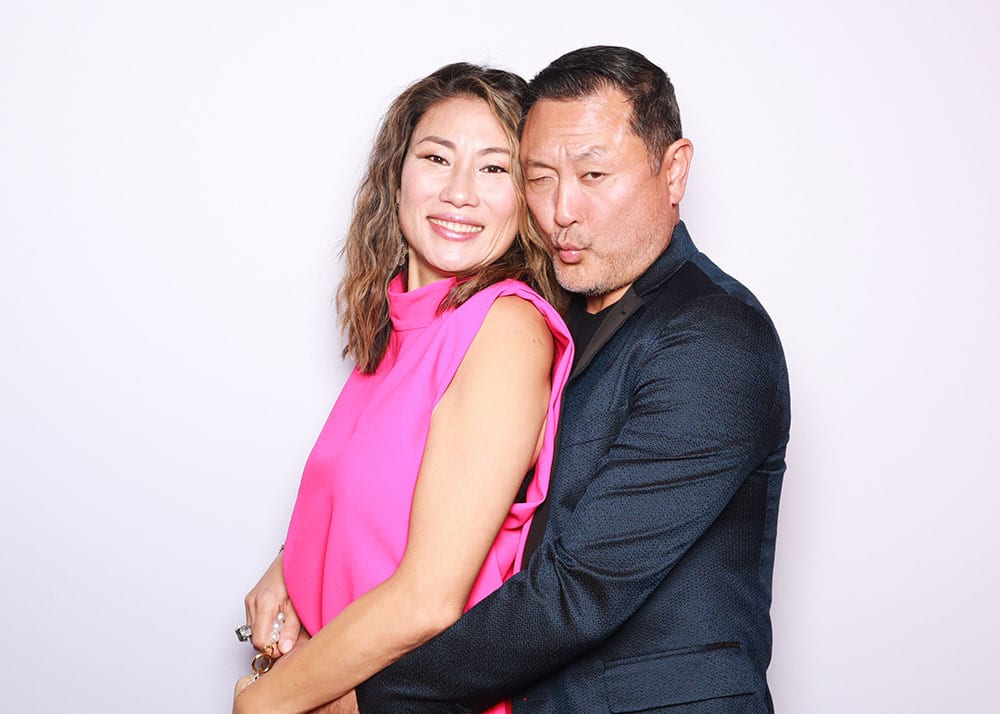 Couple posing playfully in a photo booth, featuring a woman in a pink top and a man in a dark jacket, both smiling and sharing a flirty moment, embodying the fun and romantic energy of prom-themed photo opportunities.