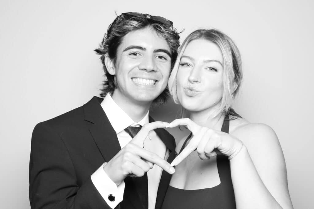 Couple posing playfully in a photo booth, forming a heart shape with their hands, showcasing love and connection, ideal for romantic moments.