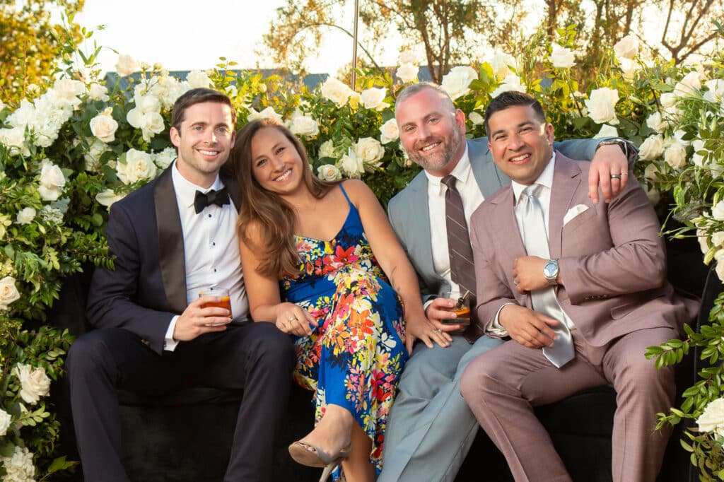 Group of four friends posing together on a couch surrounded by white roses, showcasing a festive atmosphere ideal for social media sharing and experiential marketing.