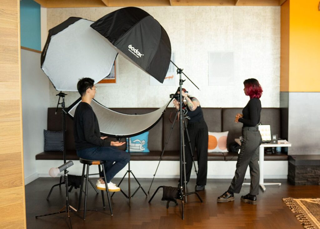Corporate event photography session with a person sitting for a headshot, surrounded by lighting equipment and photographers adjusting settings.