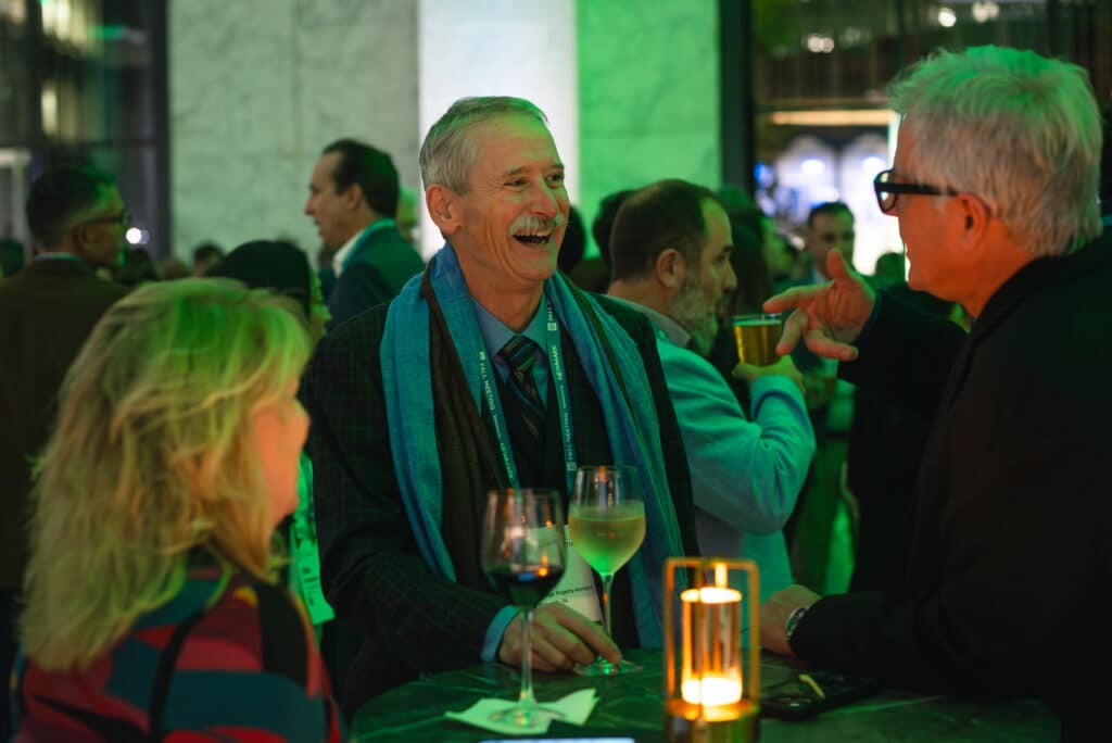 Group of people enjoying an interactive event, laughing and engaging in conversation, with drinks in hand, under ambient green lighting, showcasing experiential marketing and social interaction.