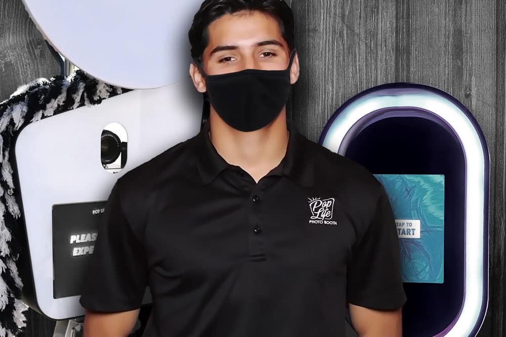 Man wearing a black mask and Pop Life Photo Booth shirt standing next to a photo booth with a "Tap to Start" sign, illustrating photo booth rental services after COVID-19.