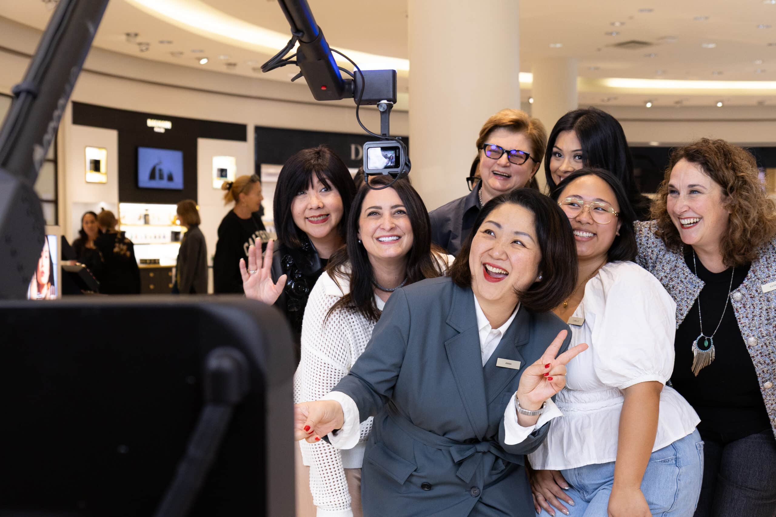 Group of women smiling and posing for a photo in a luxury retail environment, showcasing the Glambot activation at Neiman Marcus, enhancing the shopping experience with shareable content.