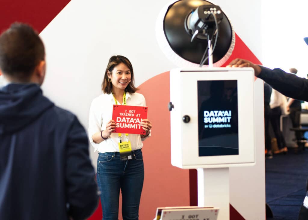Woman holding a sign and smiling for her picture to be taken with an open-air photo booth