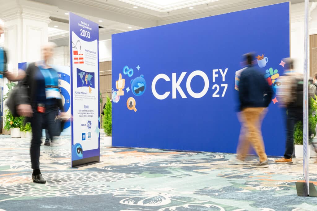 Event backdrop featuring "CKO FY 27" logo with blurred attendees, illustrating a corporate event atmosphere and the evolution of photo booth technology for experiential marketing.