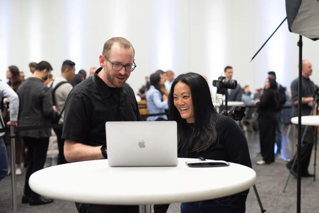 A Pop Life Photo team member and a smiling attendee review headshot results together on a laptop at the activation station, with the busy event floor visible in the background.
