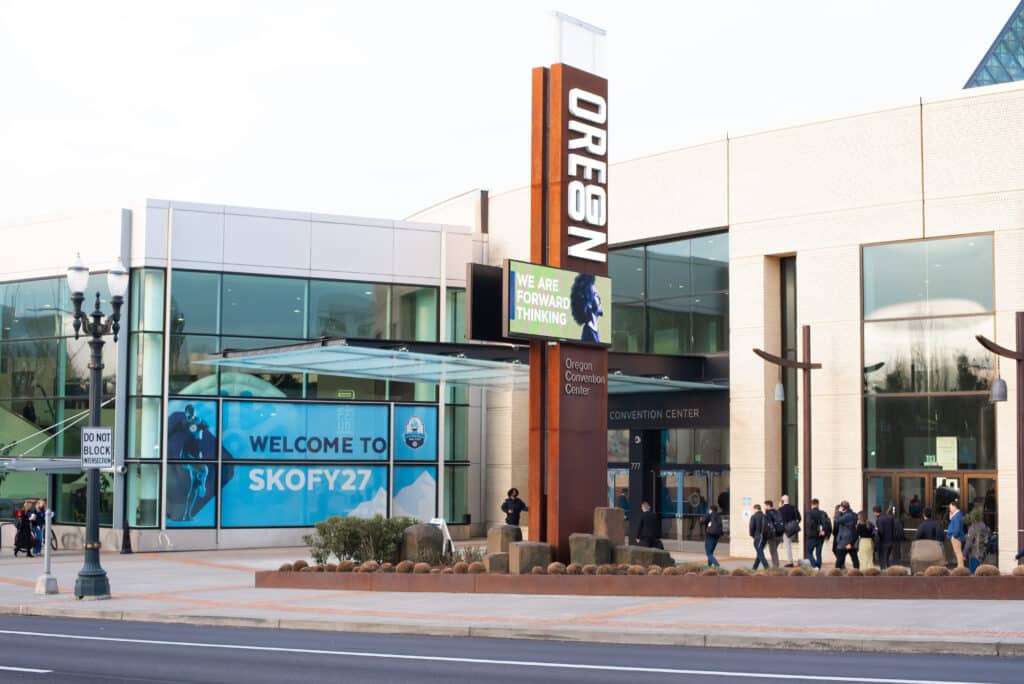 Exterior of the Oregon Convention Center with a large Snowflake SKO FY27 welcome banner displayed on the building facade and attendees arriving at the entrance.