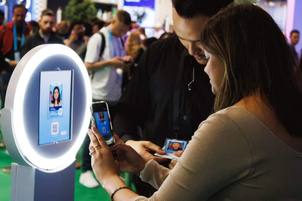 Attendee scanning a QR code with her phone at a ring-light photo booth to download her digital photo at a tech conference.